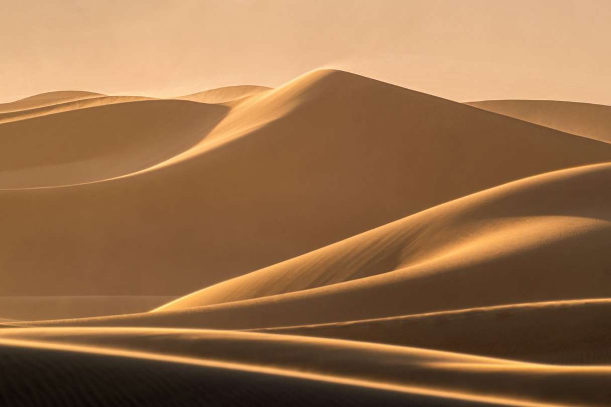 Golden sand dunes rolling into the distance under a hazy sky.